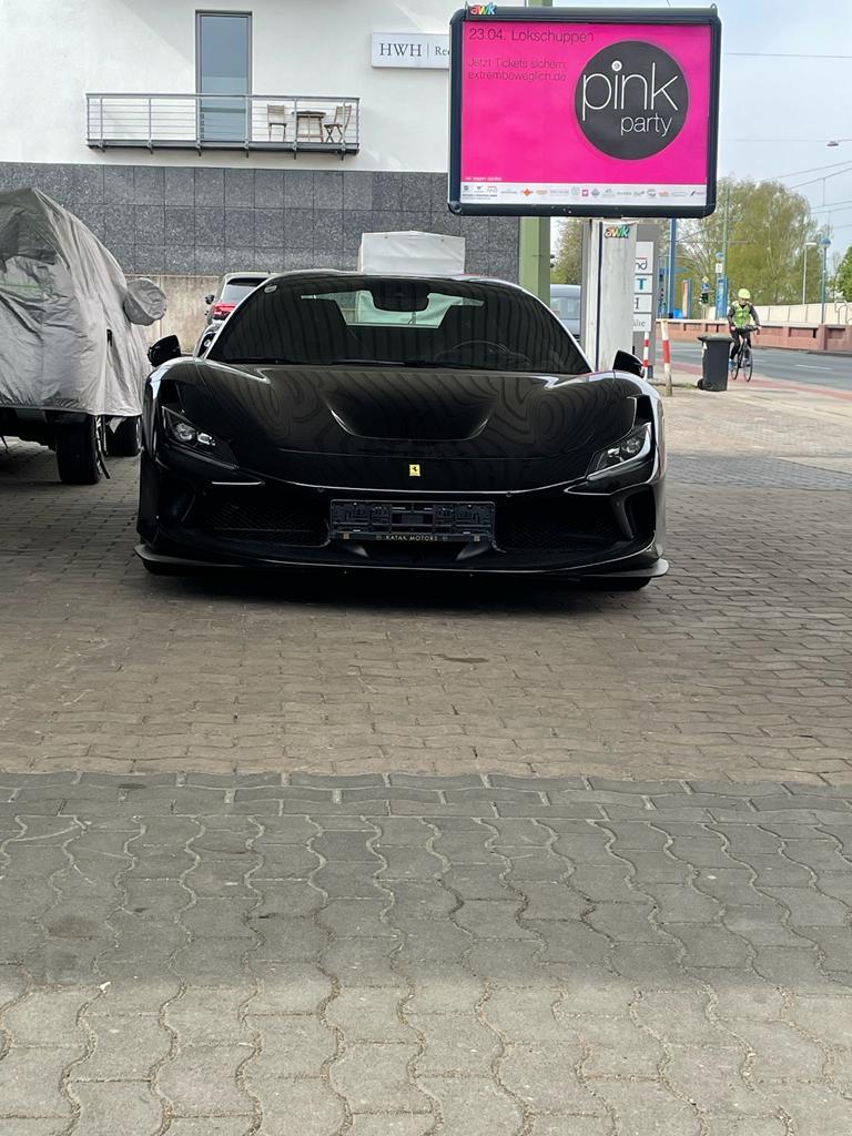 Schwarzer Sportwagen mit eleganten Linien, geparkt unter freiem Himmel, im Hintergrund ein Plakat.