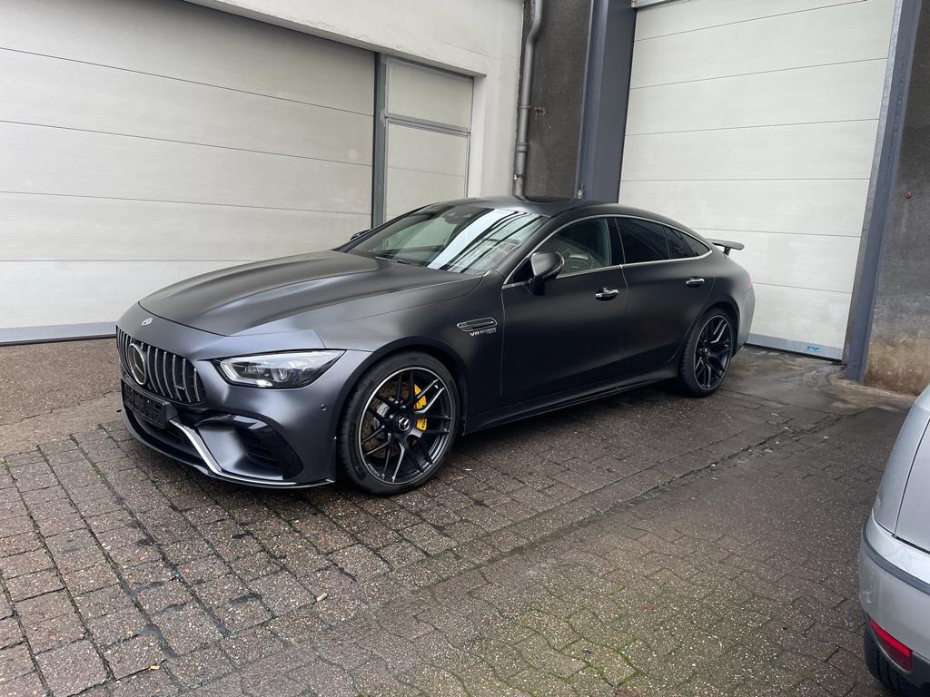 Ein mattgrauer Sportwagen mit gelben Bremssätteln, geparkt auf nassem Pflaster in einer Garage.