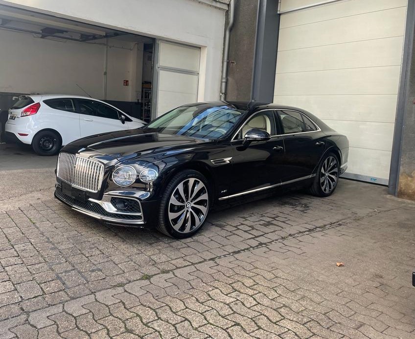Schwarzer Luxuswagen mit markantem Kühlergrill und großen Felgen, geparkt vor einer Garage.