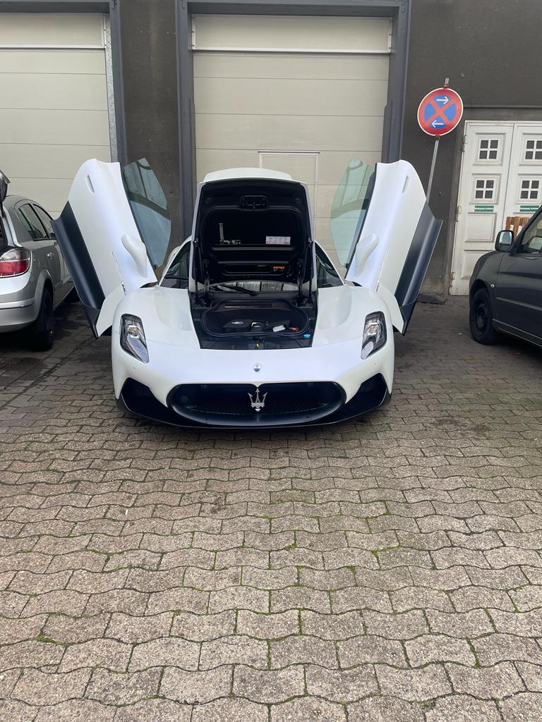 Weißer Sportwagen mit geöffneten Flügeltüren und Motorhaube, parkend auf einem Kopfsteinpflaster.